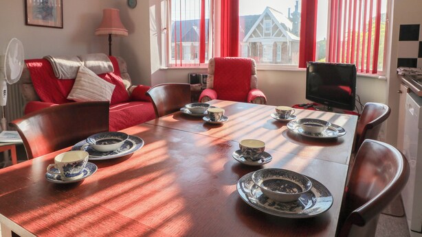 Comedor con mesa de madera dispuesta para té, cortinas rojas y vistas a casas afuera.