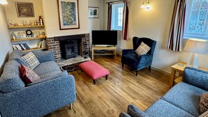A living room with a fireplace, two sofas, a TV, and a small table. - Cajun Cottage (Wareham)