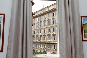 Visão através de cortinas de um edifício de vários andares com arquitetura clássica, destacando inúmeras janelas e uma entrada central.