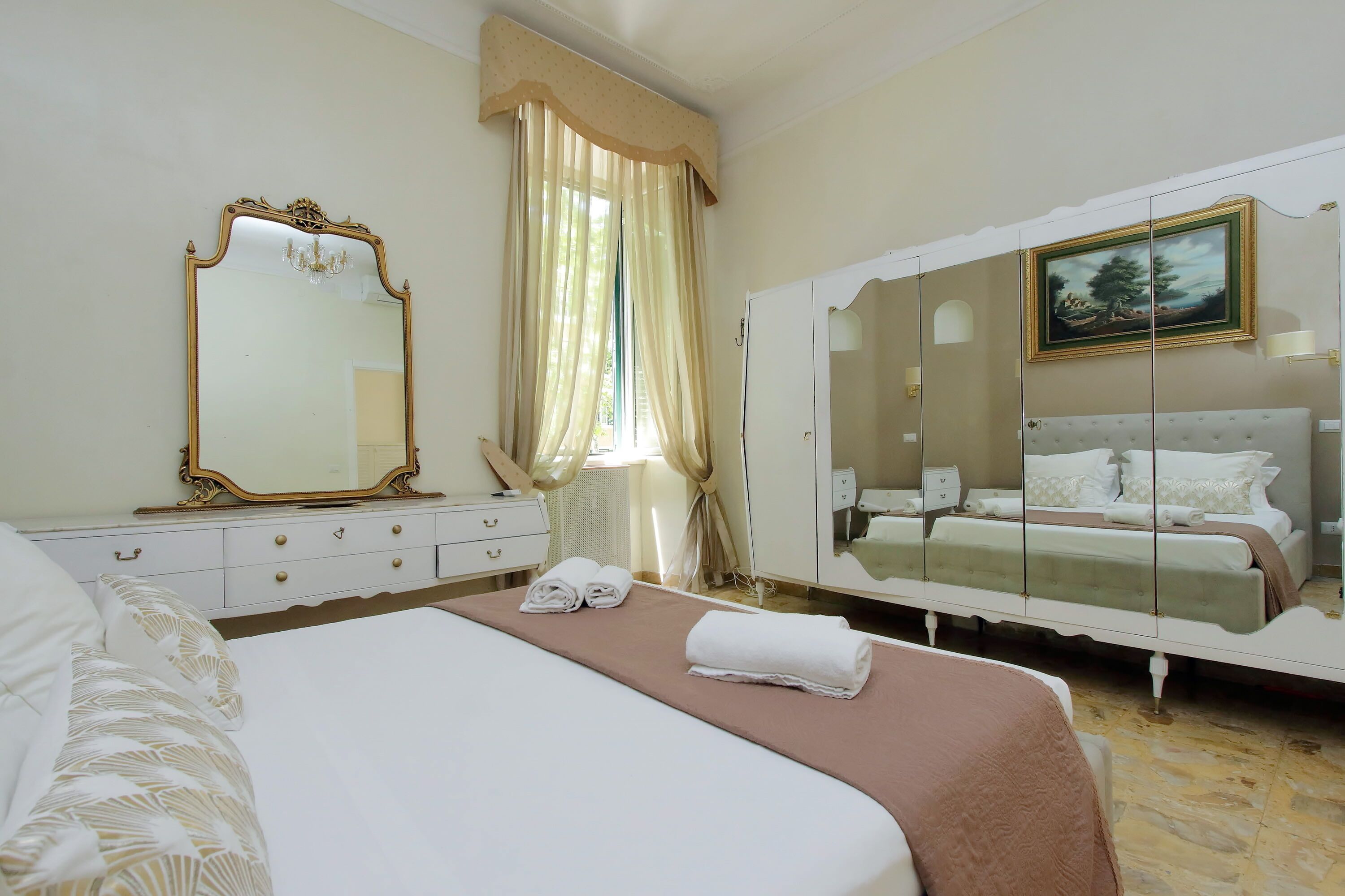Une chambre d’hôtel avec un grand lit, une armoire avec un miroir, un tableau au mur et une fenêtre avec des rideaux.