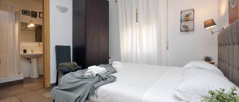 Un dormitorio con cama, armario, mesita de noche, lámpara y una planta pequeña.