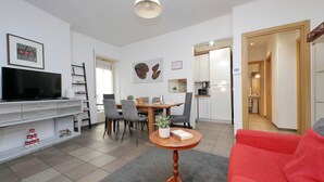 Ein modernes Wohnzimmer mit Fernseher, Essbereich, Küche und einem roten Sofa.
