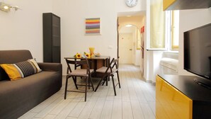 Un espacio habitable compacto con sofá, mesa de comedor, sillas, televisor y un reloj en la pared.