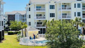 Un immeuble résidentiel à plusieurs étages, doté de balcons, d’une piscine et d’une pelouse bien entretenue.