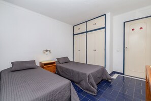 Een kamer met twee enkele bedden, een houten nachtkastje, een kledingkast met blauwe omlijsting en een deur met rode stickers.