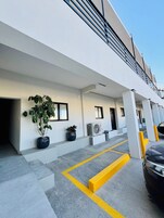 Un bâtiment moderne doté d’un parking couvert, de plantes en pot et d’une voiture.