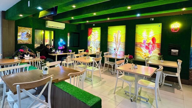 A restaurant interior with green walls, white chairs, and tables. There are paintings on the walls and a neon sign. - Capital O Hotel Jazuli, San Jose del Cabo (San José del Cabo)