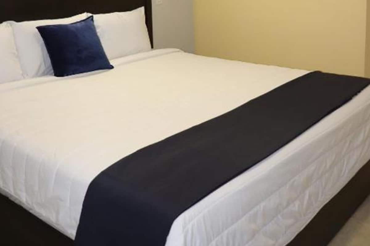 A neatly made bed with white and navy bedding, a dark headboard, and a painting of a desert landscape on the wall.