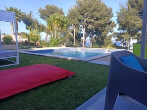 Una piscina amb un coixí vermell i una cadira, envoltada per gespa i arbres.