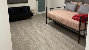 Une chambre à coucher avec un lit, un canapé, une porte et une fenêtre avec des stores.