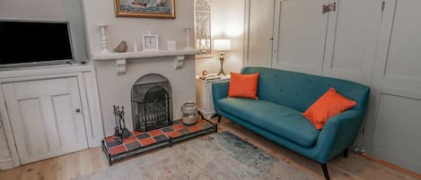 Ein Wohnzimmer mit Kamin, einem türkisfarbenen Sofa, einem farbenfrohen Teppich und einem Gemälde an der Wand.