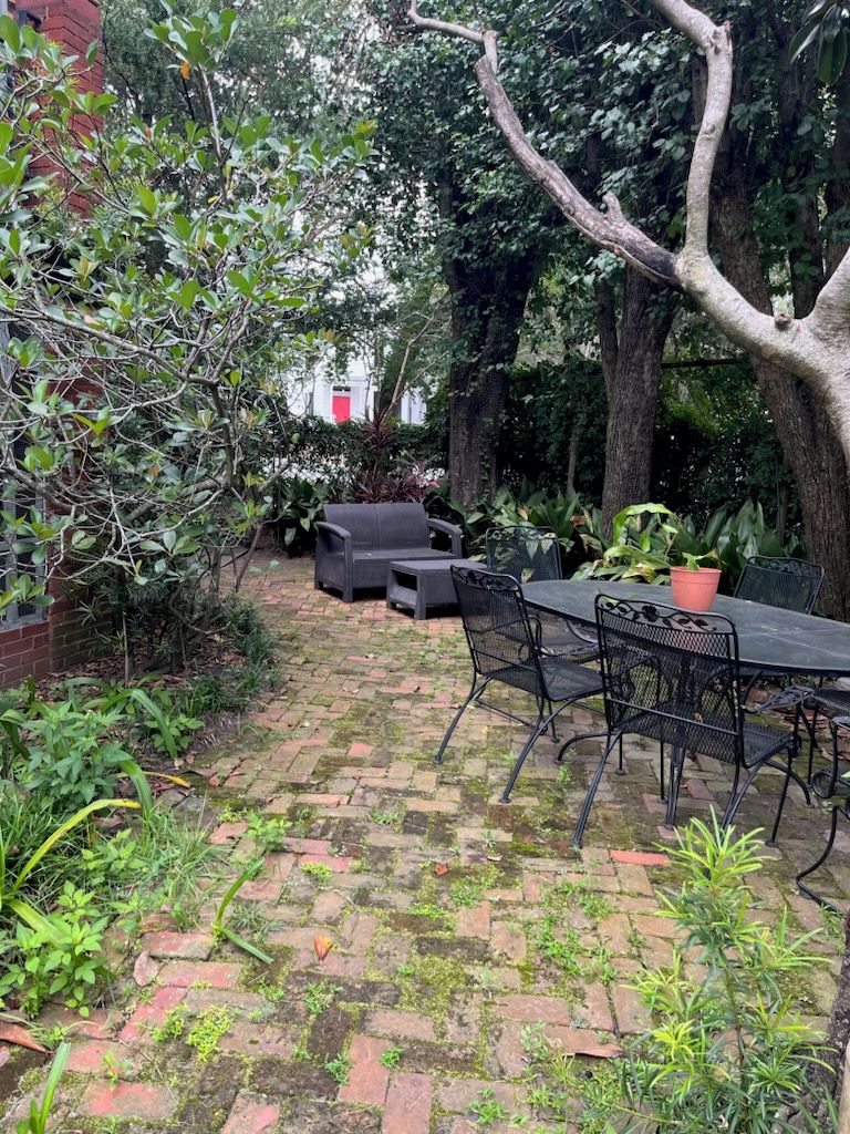 Un patio exterior con piso de ladrillo, rodeado de follaje y árboles.