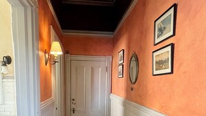 A hallway with a patterned carpet, a white door, and wall-mounted pictures. - George Baldwin House Suite (Savannah)