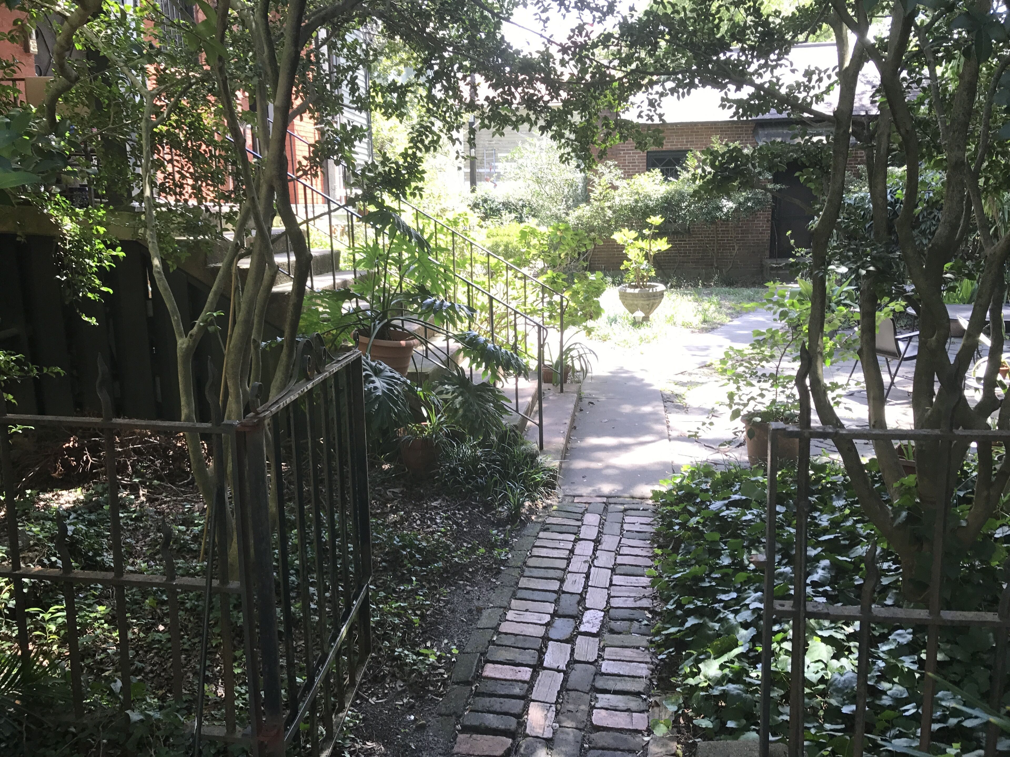 A brick pathway leading through a garden with trees and a fence.