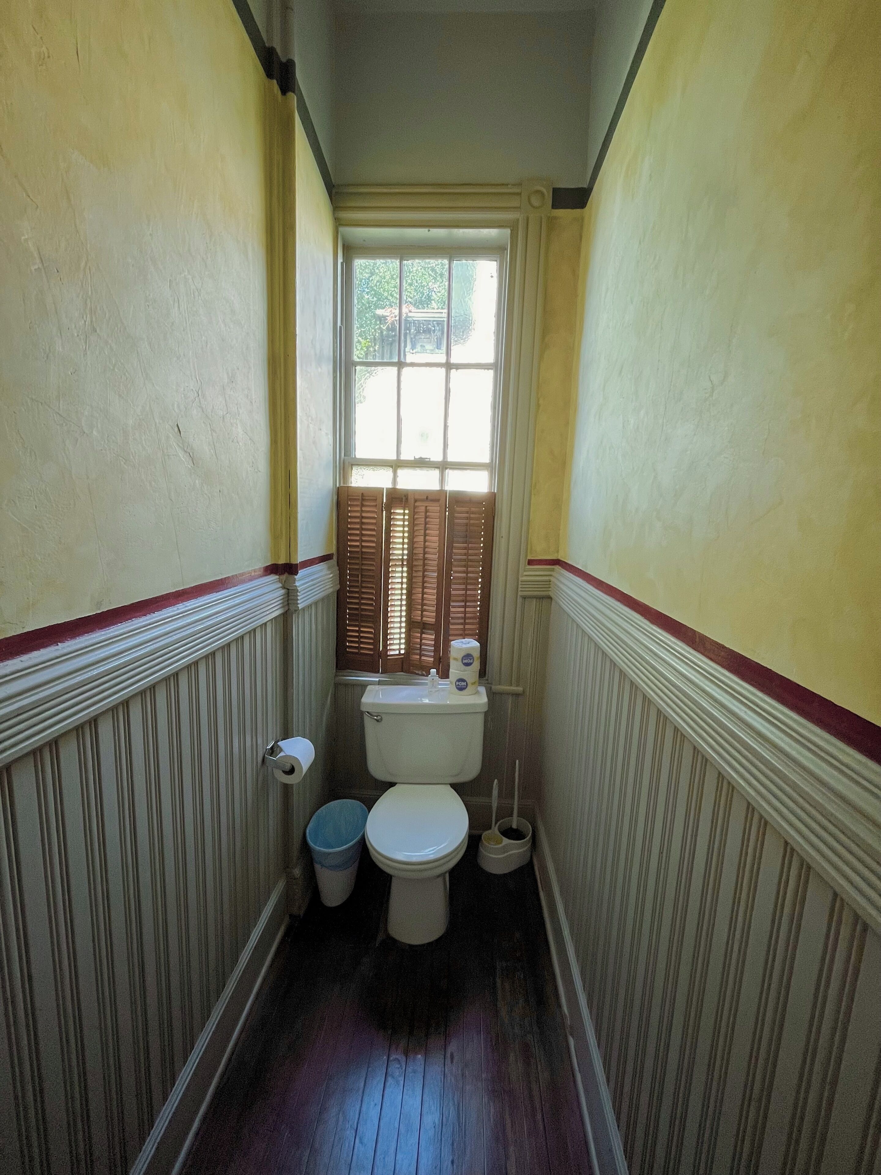 Un baño pequeño con un inodoro, dos cubetas y una ventana.