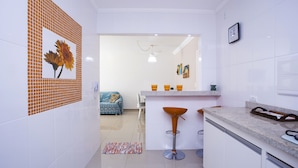 Een moderne keuken met witte tegels, een barkruk en een zithoek met een bank en vloerkleed.