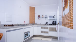 Een moderne keuken met witte kasten, een magnetron, een koffiezetapparaat en een gasfornuis.