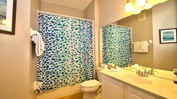 A bathroom with a shower curtain featuring a blue and green polka dot pattern, a white toilet, a sink with a mirror, and a towel rack.