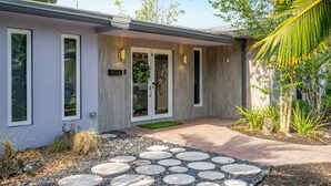 Una casa moderna con un camino de piedra que conduce a la entrada, rodeada de plantas tropicales.