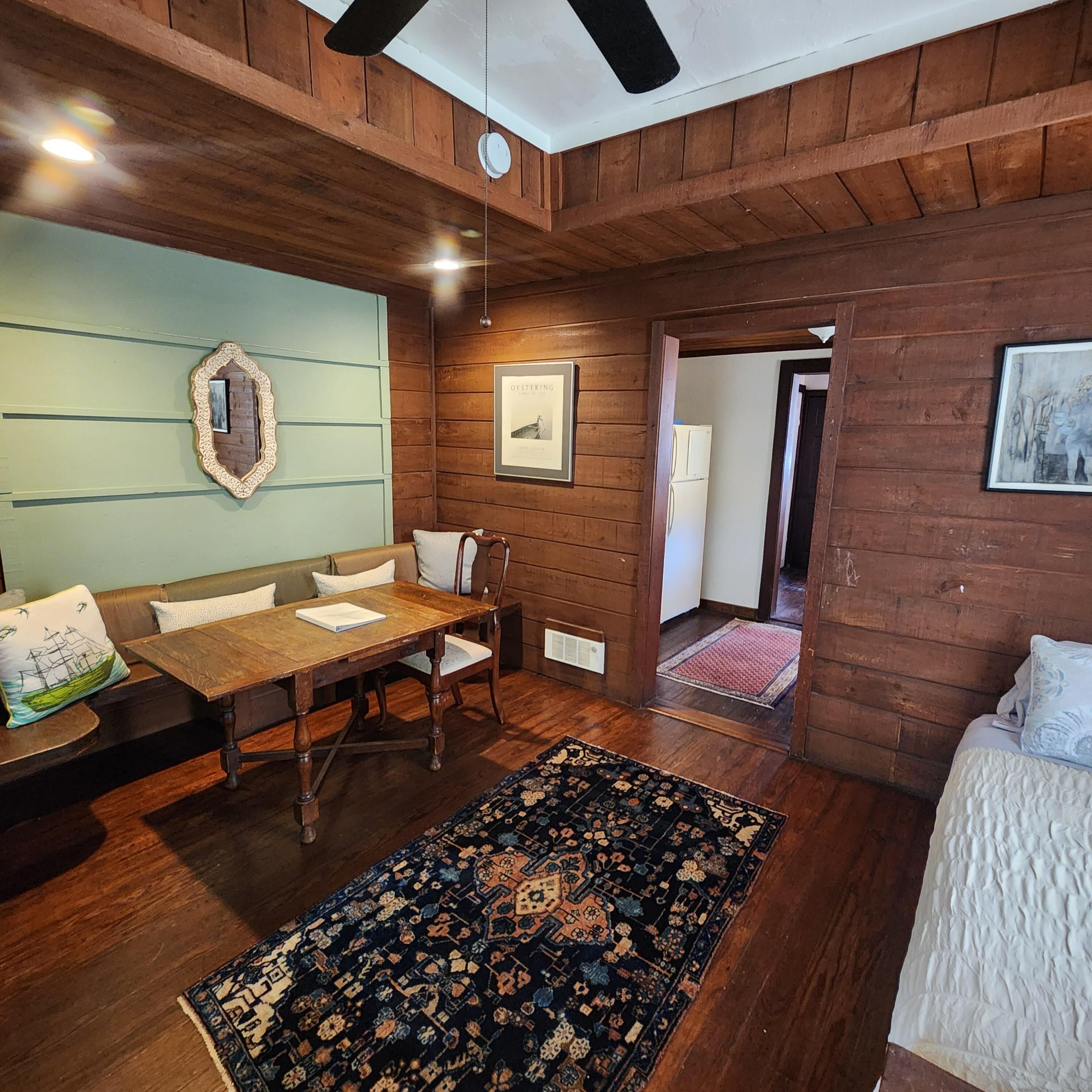 Een gezellige kamer met houten plafond, een eettafel met stoelen, een tapijt met patroon en een bed met wit dekbed.