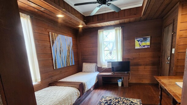Ein Zimmer in einer Holzhütte mit zwei Betten, einem Deckenventilator, einem Fernseher und einem großen Teppich.