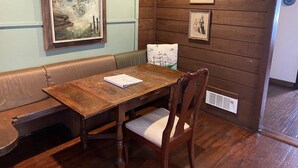 Une pièce aux murs lambrés, avec une table en bois, un banc rembourré et des œuvres d’art encadrées.