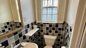 Une salle de bain avec un lavabo blanc, des toilettes et une fenêtre avec des volets.