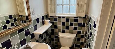A bathroom with a white sink, a toilet, and a window with shutters.