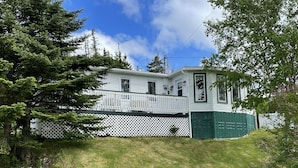 Una casa blanca con puerta verde, cerca blanca y jardín cubierto de césped.