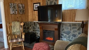 Una sala de estar acogedora con una chimenea de piedra, un televisor montado encima y un sofá cómodo.