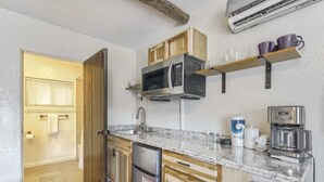 Eine kompakte Küche mit Holzausbau, einem Edelstahlkühlschrank, einer Mikrowelle, einer Kaffeemaschine und einem Spülbecken.