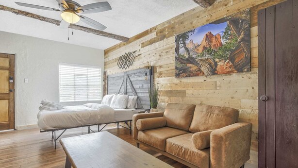 Ein Zimmer mit einem Bett, einer Couch, einem Holztisch, einem Deckenventilator und einem Bild an der Wand.