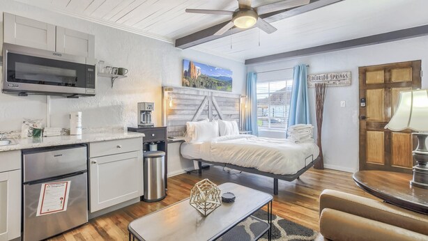 Una habitación de hotel compacta con cama, kitchenette y ventilador de techo.