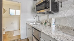 Una cocina compacta con un lavamanos de acero inoxidable, un microondas y una encimera con dispensador de toallas de papel.