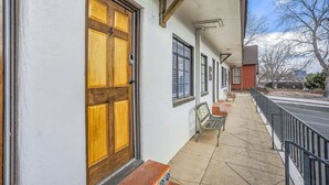 Un edificio con puerta de madera marcada con el número 4, un área de estar al aire libre techada con sillas y una acera que lleva a una calle.