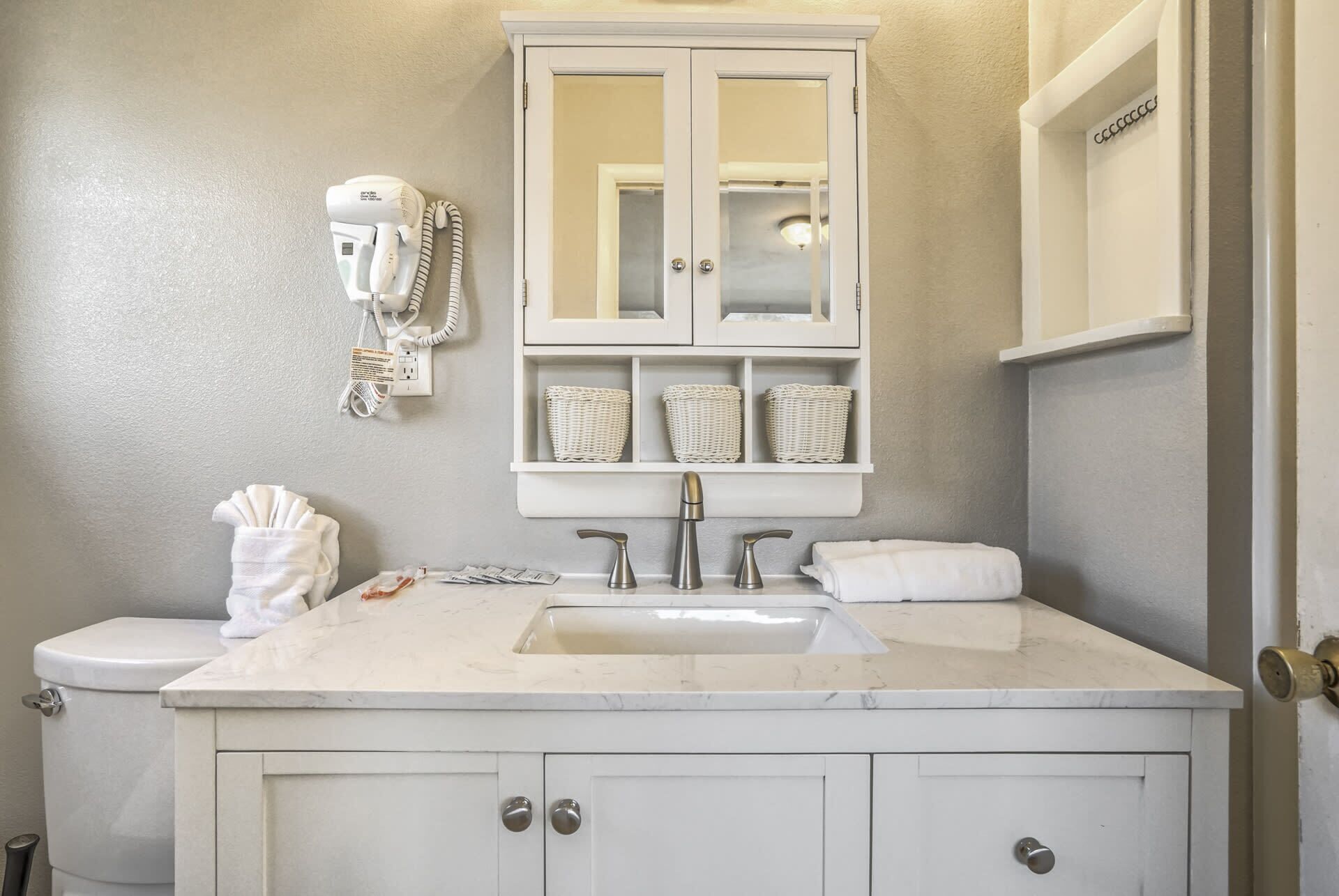 A bathroom with a white vanity, a sink, a mirror, and a hairdryer mounted on the wall.
