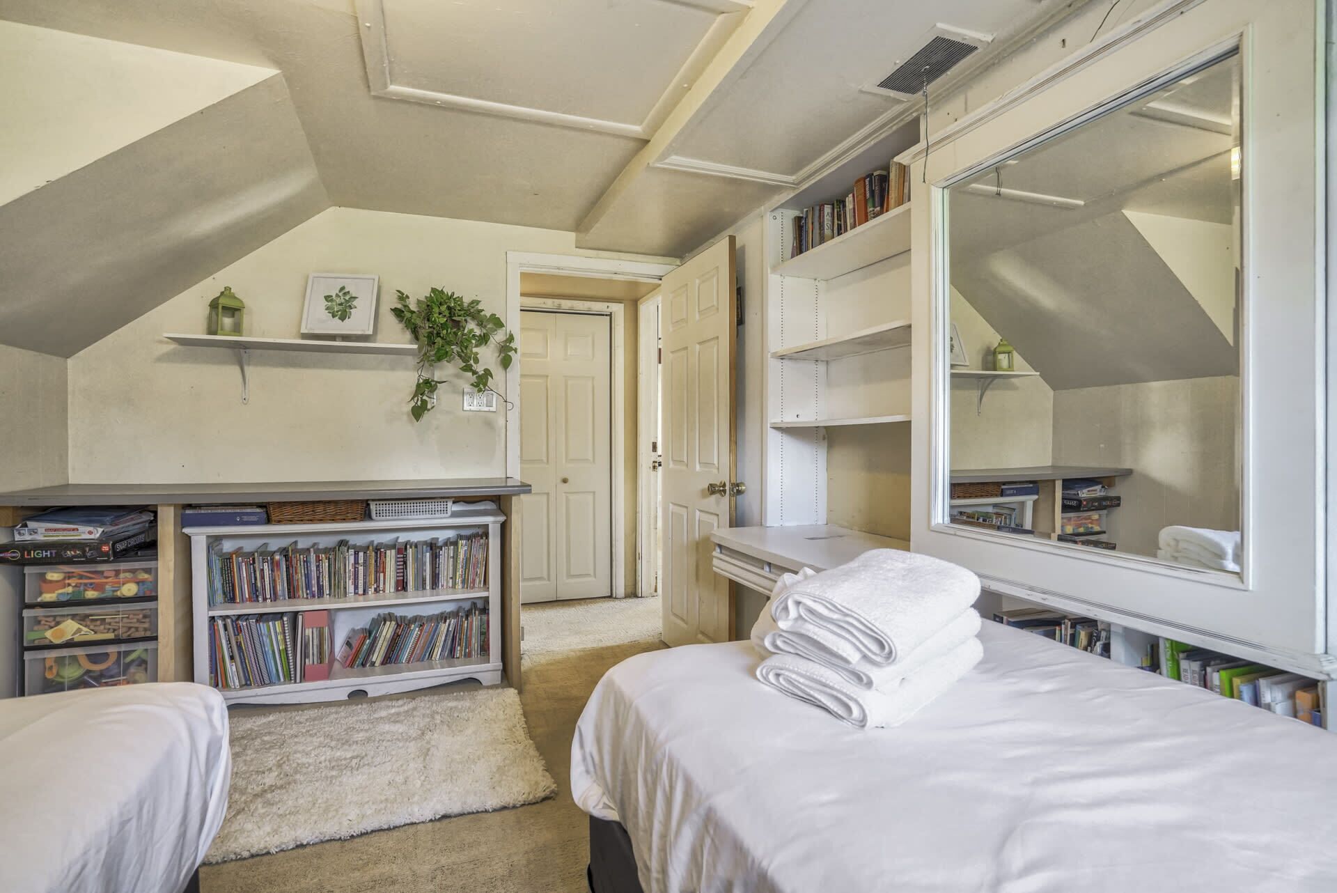 A bedroom with a large mirror, a bookshelf, a desk, and a bed with towels.