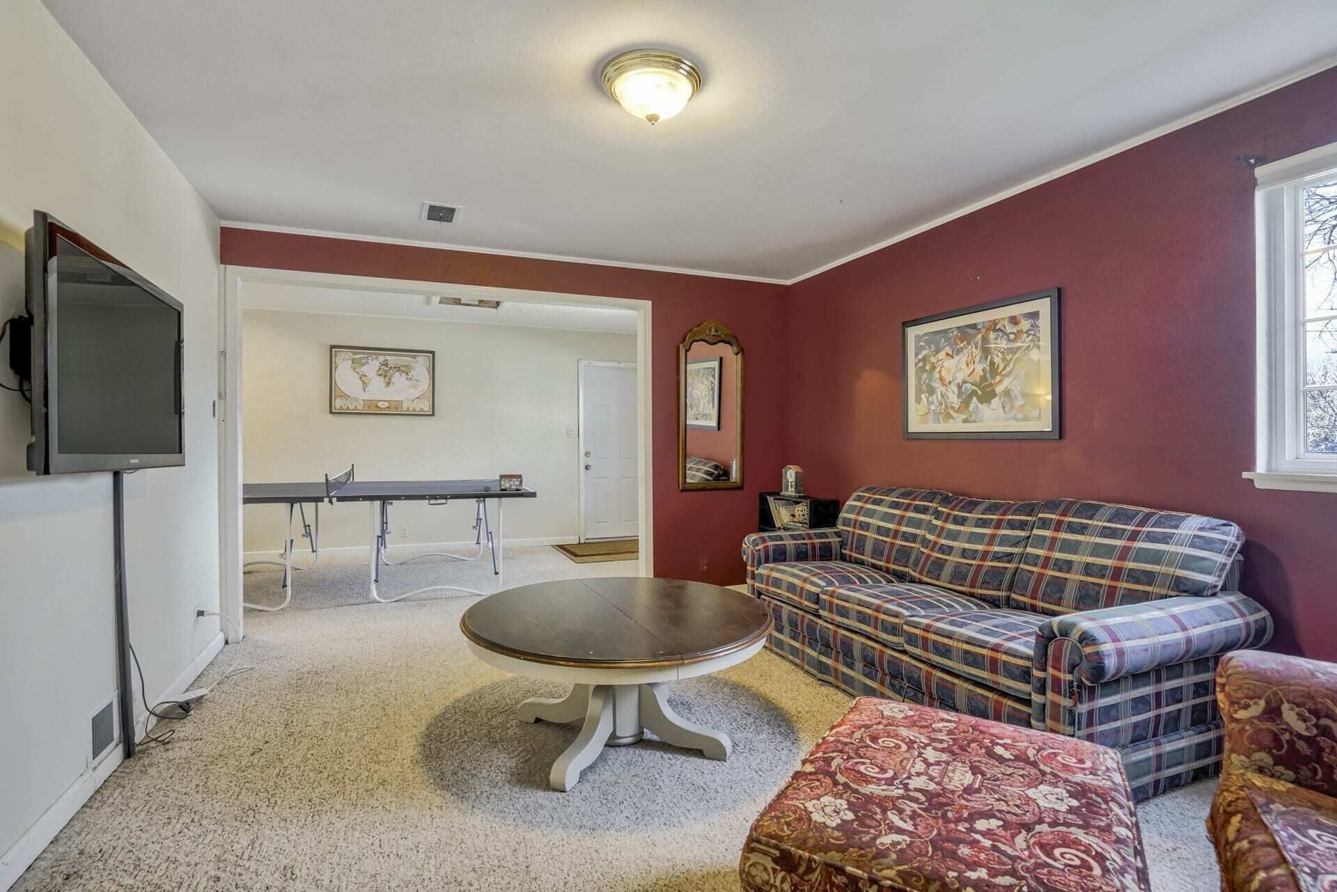 A living room with a round coffee table, a plaid sofa, and a television mounted on the wall.