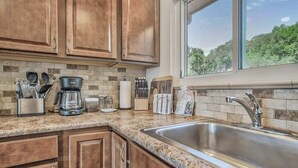A kitchen with wooden cabinets, a granite countertop, a stainless steel sink, and a window with a view of trees.