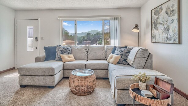 A living room with a sectional sofa, a round wicker coffee table, and a small side table with decorative items.