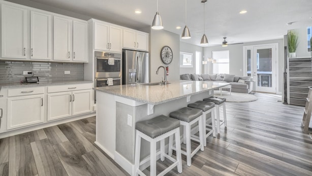 A modern kitchen with white cabinets, stainless steel appliances, and a central island with bar stools. - 3BD Rooftop Lounge Restaurants & Parks (Castle Rock)
