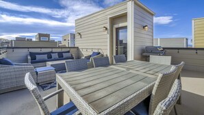 A rooftop patio with wicker furniture, a grill, and a door leading to an upper level. - 3BD Rooftop Lounge Restaurants & Parks (Castle Rock)