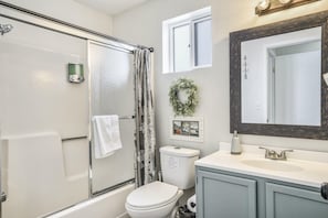 Une salle de bain avec une douche à parois de verre, des toilettes, un lavabo avec un miroir et un petit tableau encadré accroché au mur.