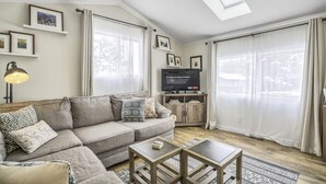 A living room with a sofa, coffee table, and TV. There are curtains, a lamp, and framed pictures on the wall. - 3bd1 Mile to Garden of the Godstraveler's Home (Colorado Springs)