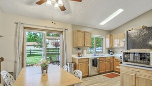 Une cuisine avec des meubles de rangement en bois, une table à manger avec des chaises, un réfrigérateur et un ventilateur de plafond.