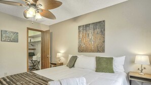Une chambre d’hôtel avec un grand lit, un ventilateur de plafond, un tableau au mur et une petite table avec une lampe.