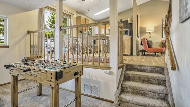 Une pièce avec une table de baby-foot, un escalier et une vue sur un balcon aménagé avec du mobilier d’extérieur.