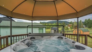 Un bain à remous installé sous une pergola, avec vue sur un bâtiment verdoyant et une structure en bois en arrière-plan.