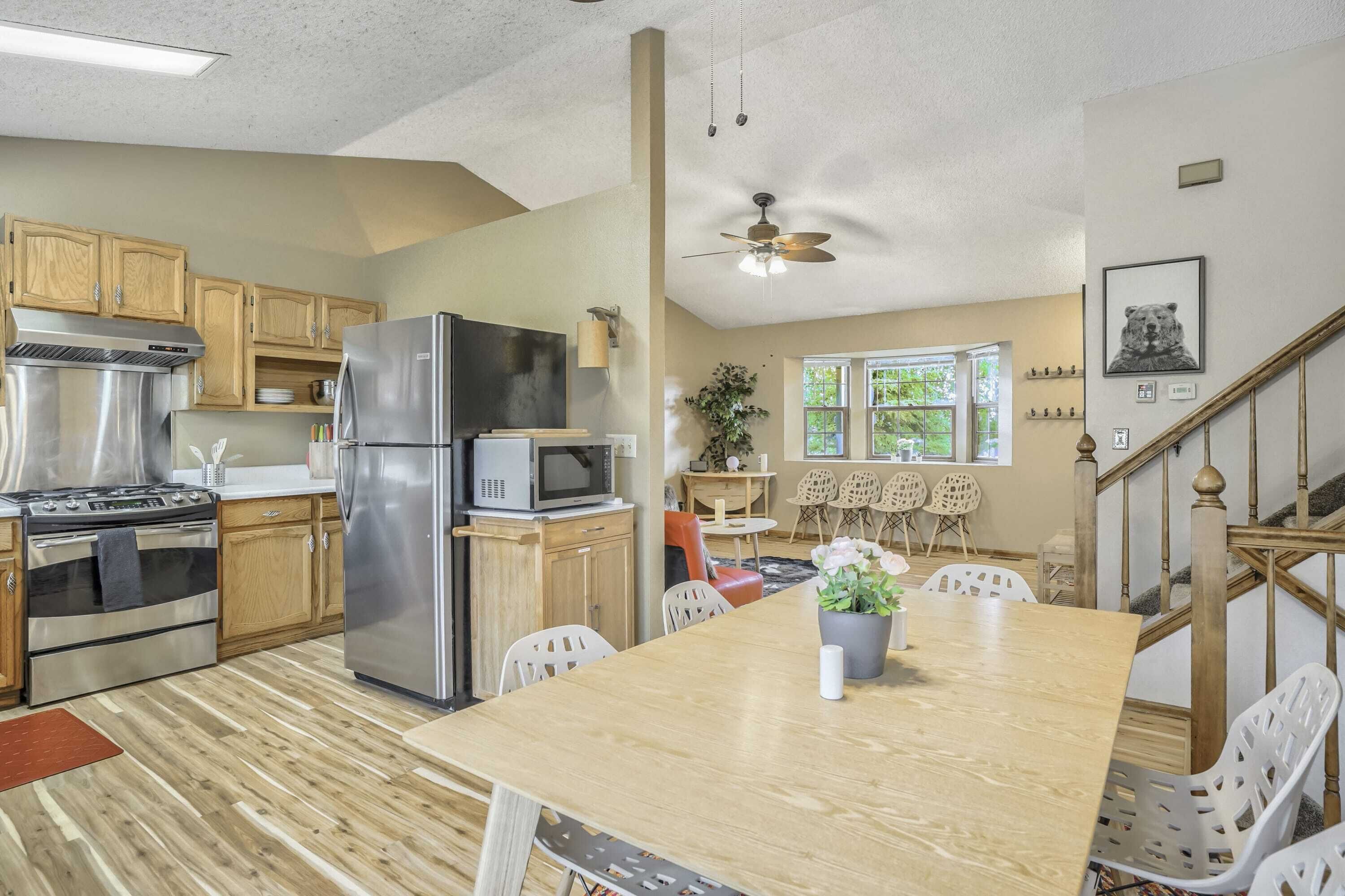 A modern kitchen with stainless steel appliances, wooden cabinets, and a dining area with a wooden table and white chairs.