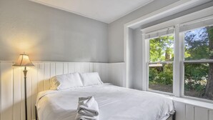 A neatly made bed with white linens and a folded towel, a floor lamp, and a window with a view of greenery outside. - 3bdcheyenne Mtn Suburbsrestaurants & Hiking (Colorado Springs)